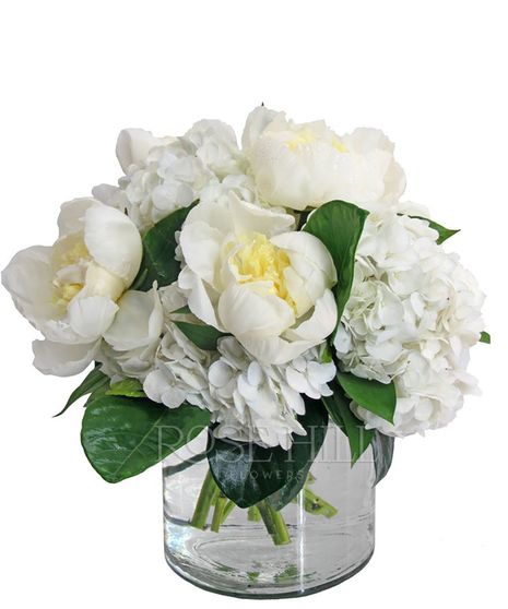 Peonies and white hydrangea with green accents in a round glass vase