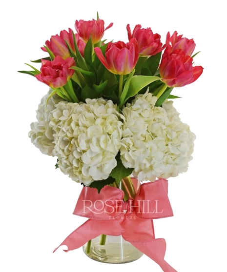 Tulips and hydrangea in a glass vase tied with a bow.