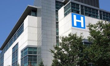 A large modern hospital building displays a prominent blue sign with a white 